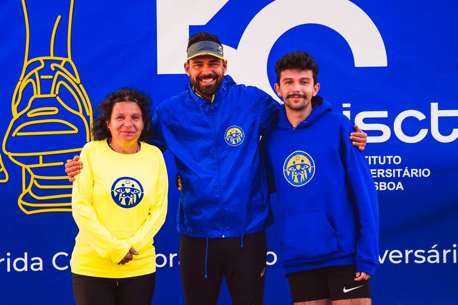 Three people smiling and posing in front of a sports event backdrop wearing athletic clothing.
